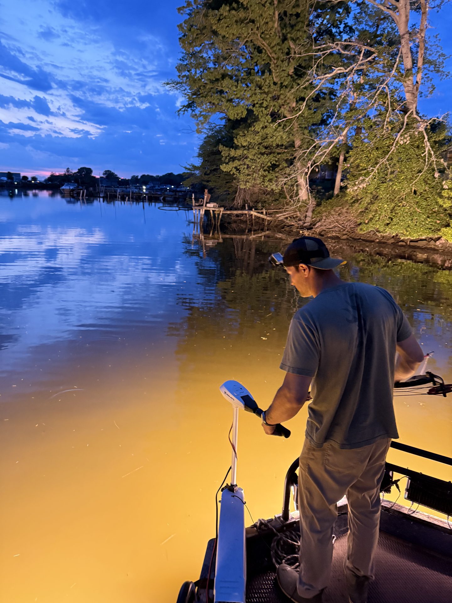 Bowfisherman on a lit shooting deck at dusk on a Maryland creek