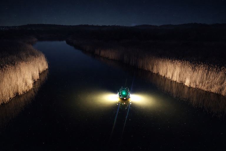 The bowfishing rig lit up on a narrow, dark creek at night